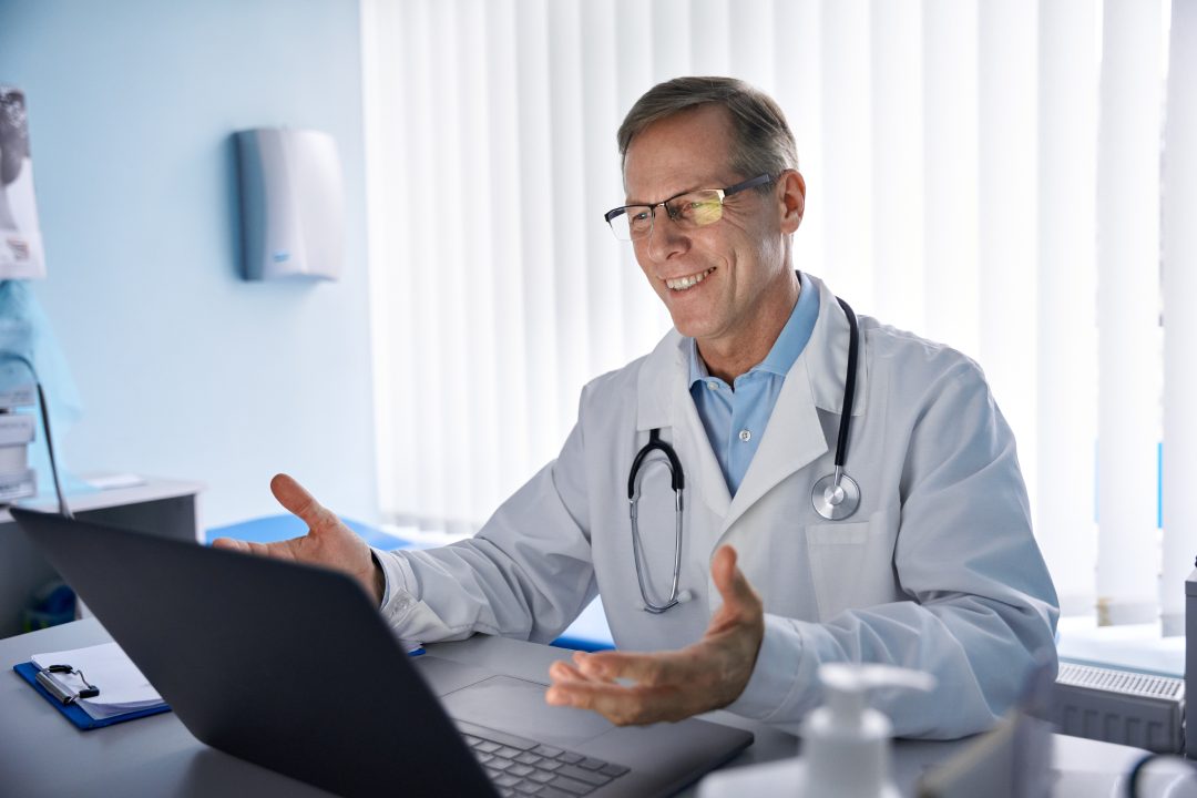 Happy old male doctor physician talking, consulting patient online by webcam video call on laptop computer. Telemedicine conference virtual tele meeting. E appointment, telehealth zoom therapy.